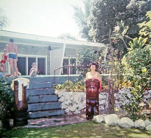 Jean stands behind a tikki in front of the pool at Aggie Greys.